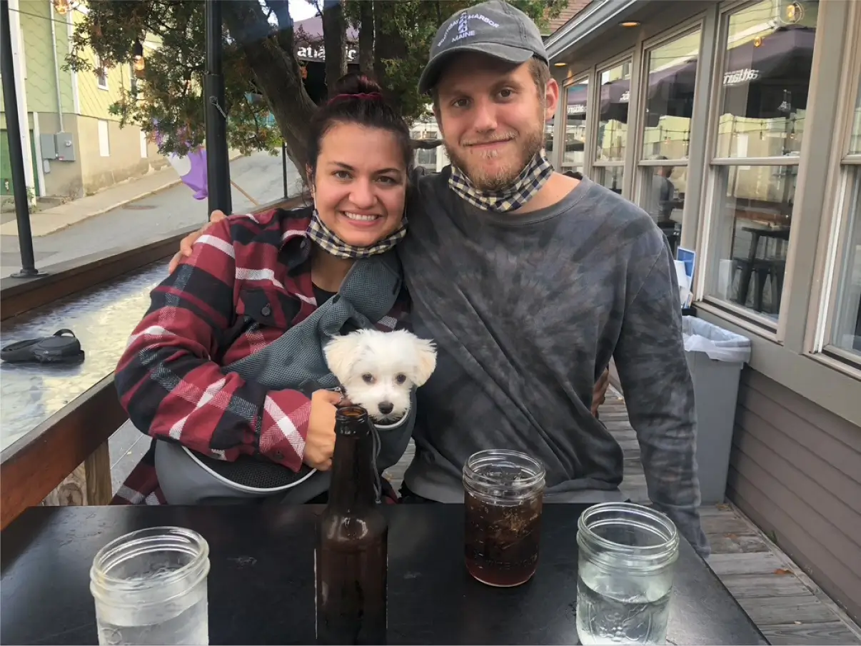 Alissa and Matt at a restaurant table outdoors with their dog Koia in a carrier bag